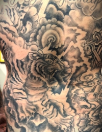 Ausschnitt eines großflächigen japanischen Rückentattoos in Black-and-Grey. Zu sehen ist ein detailreich gestreifter, brüllender Tiger (Tora) inmitten von traditionellen, dunkel schattierten Sturmwolken und scharfkantigen, hellen Blitzen, gestochen von BIG WAVE TATTOO PRIVATE & ART.