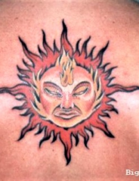 Nahaufnahme eines auf dem oberen Rücken tätowierten Sonnensymbols im Traditional-Stil, das ein ausdrucksstarkes Gesicht im Zentrum zeigt, umgeben von wilden, rot-schwarz schattierten Flammenstrahlen, gestochen von BIG WAVE TATTOO PRIVATE & ART. Traditional Tattoo mit Sonnensymbol