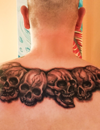 Symmetrisches Rücken-Tattoo eines Mannes, das eine Kette aus mehreren aneinandergereihten, detailreich schattierten Totenköpfen im Black-and-Grey-Stil über die gesamte Schulterlinie zeigt, gestochen von BIG WAVE TATTOO PRIVATE & ART.