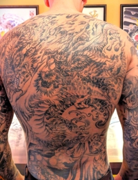 Ein vollständig tätowierter Rücken (Full Backpiece) im traditionellen japanischen Irezumi-Stil. Zu sehen ist ein detailreicher, riesiger japanischer Drache (Ryu) in feinen Black-and-Grey-Schattierungen. Der Körper des Drachen windet sich zwischen detailgetreuen Wellen, Wolken und Gischt-Elementen über den gesamten Rücken und verbindet sich mit den Armtattoos, gestochen von BIG WAVE TATTOO PRIVATE & ART.