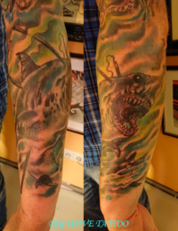 Zwei Ansichten eines Arm-Tattoos im traditionellen Stil im direkten Vergleich. Zu sehen ist ein bedrohlicher Hai mit weit geöffnetem Maul und spitzen Zähnen, der von einer Harpune oder Lanze getroffen wurde. Der Fisch schwimmt in einem stürmischen, grün-türkis und gelb schattierten Wellen- und Wolkenhintergrund, gestochen von BIG WAVE TATTOO PRIVATE & ART.