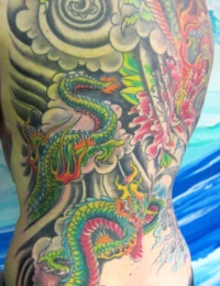 Ein vollständig tätowierter Rücken (Full Backpiece) im traditionellen japanischen Stil. Zu sehen sind zwei detailreiche Drachen (Ryu) mit leuchtend grünen Schuppen, gelben Bäuchen und roten Akzenten. Der Hintergrund besteht aus klassischen, dicht schattierten schwarzen Sturmwolken-Wirbeln und einer großen pinken Pfingstrose auf der rechten Rückenseite, gestochen von BIG WAVE TATTOO PRIVATE & ART.