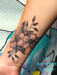 Feines florales Tattoo auf dem Unterarm einer Frau knapp über dem Handgelenk. Das Motiv zeigt zwei detaillierte Blüten mit dunkler schattierten Blättern und feinen, geschwungenen Zweigen, gestochen im eleganten Black-and-Grey-Stil von BIG WAVE TATTOO PRIVATE & ART.
