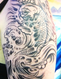 Detailansicht eines japanischen Oberarm-Tattoos in Black-and-Grey. Zu sehen ist ein aufwärts schwimmender Koi-Karpfen mit detailreichen Schuppenstrukturen inmitten von traditionell schattierten, wirbelnden Wellen und hell ausgesparten Kirschblüten (Sakura), gestochen von BIG WAVE TATTOO PRIVATE & ART.