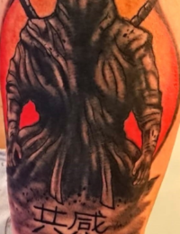 Ein Tattoo im japanischen Stil, das einen Ninja oder Samurai in dunkler Kleidung mit zwei gekreuzten Katanas auf dem Rücken zeigt. Im Hintergrund steht eine große, rot-orangefarbene Sonne. Unten sind deutliche japanische Schriftzeichen (Kanji) in rauchige Schattierungen eingearbeitet, gestochen von BIG WAVE TATTOO PRIVATE & ART.