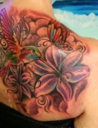 Großflächiges Lilien-Tattoo mit Kolibri und Schmetterling auf der Schulter – gestochen von BIG WAVE TATTOO PRIVATE & ART.