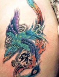Detailreiches japanisches Tattoo eines Phönix (Hōō) in leuchtendem Grün und Türkis mit einem bunten Federschweif. Der Vogel fliegt durch traditionelle, schattierte Wolken, in deren Mitte ein schwarzes japanisches Schriftzeichen (Kanji) zu sehen ist, gestochen von BIG WAVE TATTOO PRIVATE & ART.