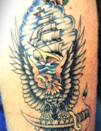 Nahaufnahme eines farbigen Arm-Tattoos im Traditional-Stil, das ein stolzes Segelschiff vor hellblauen Wolken zeigt, darunter ein detailreicher Adler mit ausgebreiteten Flügeln, der auf einem verzierten Dolch sitzt, gestochen von BIG WAVE TATTOO PRIVATE & ART.