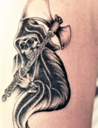 Nahaufnahme eines Arm-Tattoos im Traditional-Stil, das eine schattierte Sensenmann-Figur (Grim Reaper) in einer dunklen Kutte zeigt, die eine große, verzierte Streitaxt schultert, gestochen von BIG WAVE TATTOO PRIVATE & ART.