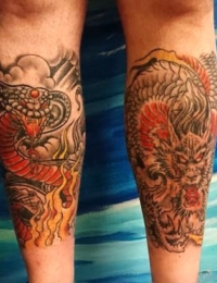 Zwei kraftvolle Tätowierungen im japanischen Stil: Das linke Motiv zeigt eine angreifende Kobra (Hebi) mit rot-orangem Körper inmitten von lodernden gelben Flammen und dunklen Sturmwolken. Das rechte Motiv zeigt das detailreiche Gesicht eines traditionellen japanischen Drachen (Ryu) in präzisen Black-and-Grey-Schattierungen mit markanten roten Akzenten an den Schuppen, gestochen von BIG WAVE TATTOO PRIVATE & ART.