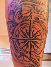 Tattoo im traditionellen Black-and-Grey-Stil auf einem Arm oder Bein. Im Mittelpunkt steht eine große Kompassrose mit einem Anker im Vordergrund. Darüber springt ein detailreich schattierter Schwertfisch (Marlin) aus peitschenden Meereswellen, gestochen von BIG WAVE TATTOO PRIVATE & ART.