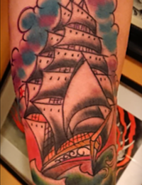 Farbenfrohes Traditional Tattoo eines dreimastigen Segelschiffs auf stürmischer See mit grünen Wellen und blau-violetten Wolken im Hintergrund, gestochen von BIG WAVE TATTOO PRIVATE & ART in Essen.