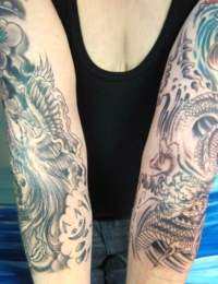 Zwei tätowierte Unterarme im japanischen Irezumi-Stil: Der linke Arm zeigt einen detailreichen Phönix (Hōō) mit Wolkenstrukturen und einer kleinen, integrierten Grinsekatze. Der rechte Arm zeigt einen traditionellen japanischen Drachen (Ryu) inmitten von dynamischen, wilden Wellen. Beide Tattoos sind in feinen Black-and-Grey-Schattierungen gestochen von BIG WAVE TATTOO PRIVATE & ART.