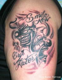 Nahaufnahme eines Oberarm-Tattoos im Black-and-Grey-Stil, das zwei Clownsmasken zeigt – eine lachend und eine weinend – kombiniert mit dem geschwungenen Schriftzug „Smile Now“ und „Cry Later“, gestochen von BIG WAVE TATTOO PRIVATE & ART.
