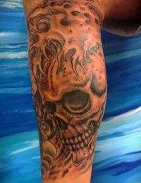 Nahaufnahme eines auf dem Bein tätowierten Schädels im Traditional-Stil, der von detailreichen, dunkel schattierten Meereswellen und Gischt umschlungen wird, gestochen von BIG WAVE TATTOO PRIVATE & ART.