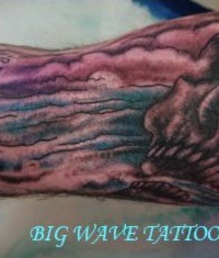 Detailliertes Black-and-Grey-Tattoo eines Schädels, der in eine dynamische, farbige Meereswelle in Blau- und Violetttönen übergeht, gestochen auf dem Arm bei BIG WAVE TATTOO PRIVATE & ART in Essen.