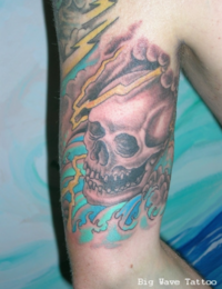 Nahaufnahme eines auf dem Arm tätowierten Totenkopfs im Traditional-Stil, der von dunklen Gewitterwolken, gelben Blitzen und türkisfarbenen Meereswellen umgeben ist, gestochen von BIG WAVE TATTOO PRIVATE & ART.